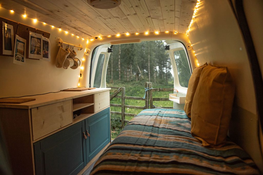 Intérieur cosy d'un van aménagé avec guirlande lumineuse, lit et rangements en bois