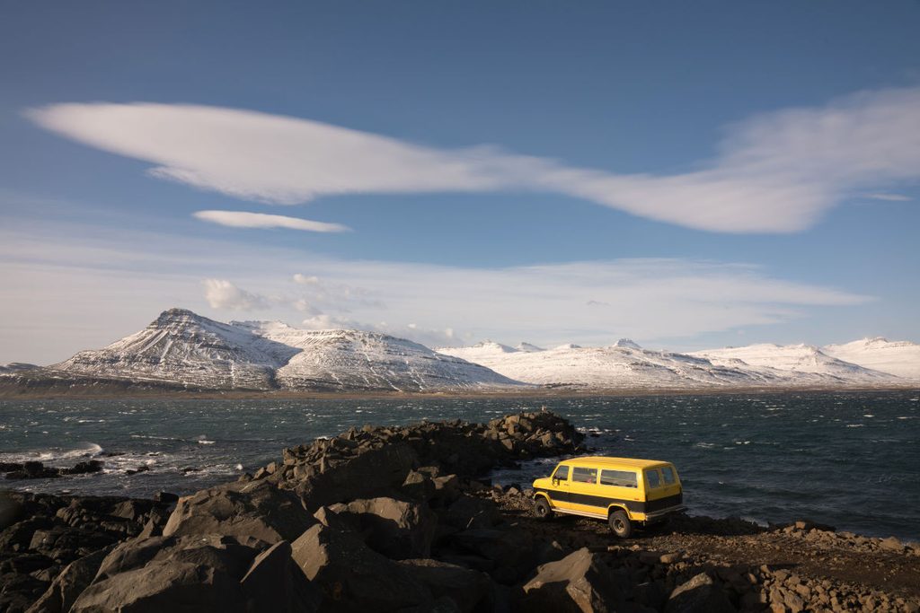 Van jaune garé sur une côte rocheuse face à des montagnes enneigées, road trip en van pas cher