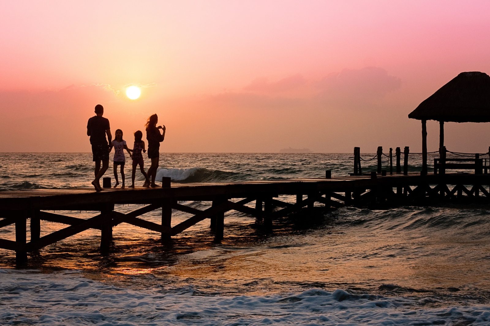 Famille avec deux enfants sur un ponton en bois au coucher du soleil, au bord d'une plage tropicale