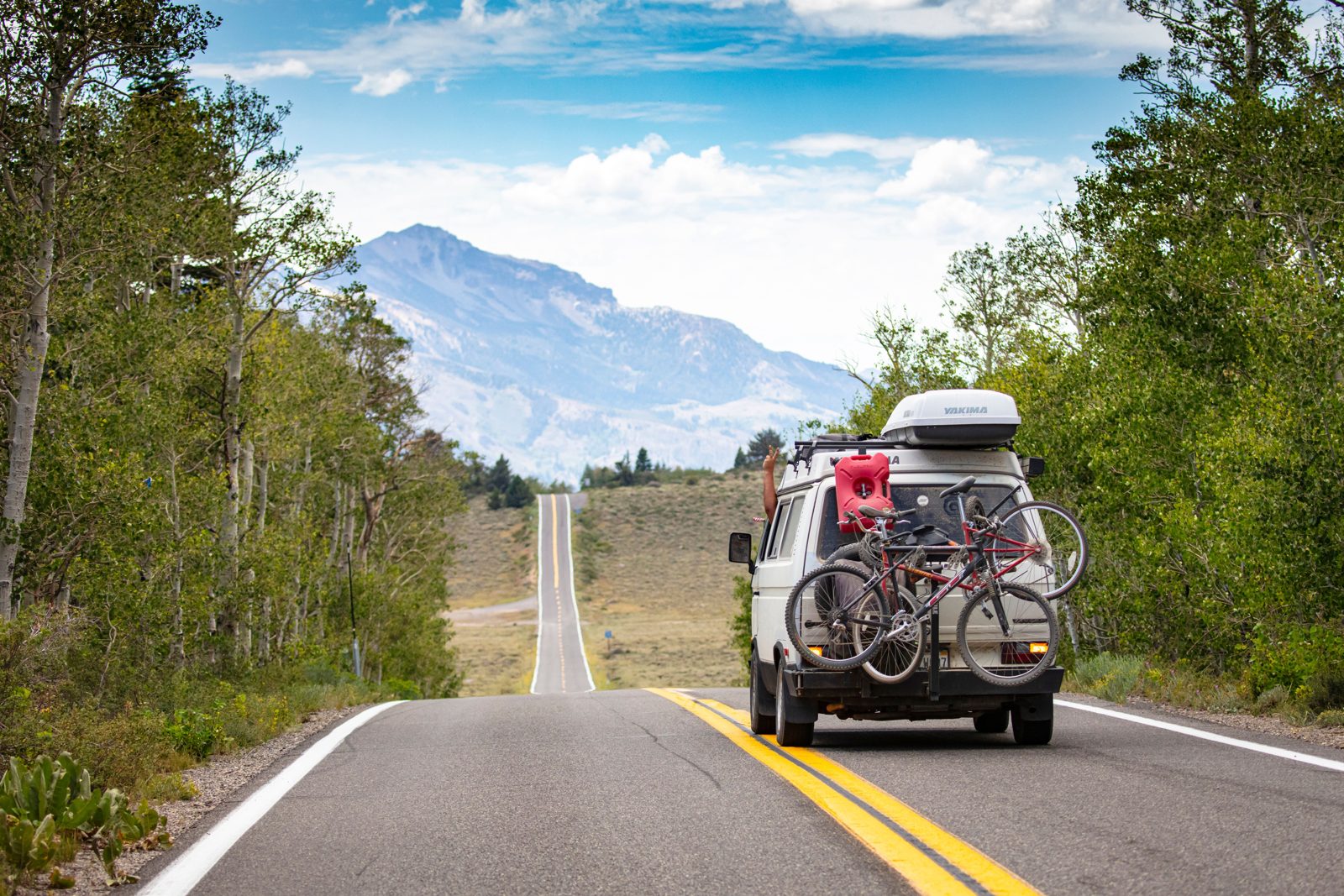Van avec vélos et coffre de toit sur une route de montagne, pendant un road trip en famille