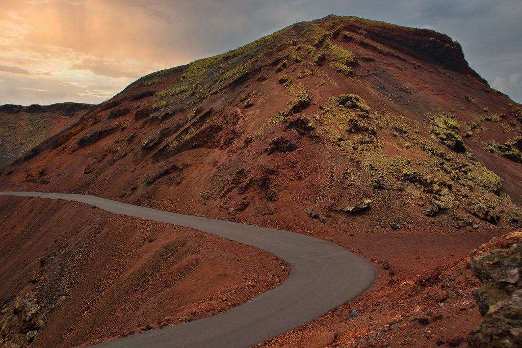 Route sinueuse traversant un paysage volcanique aux terres rouges, typique des Canaries