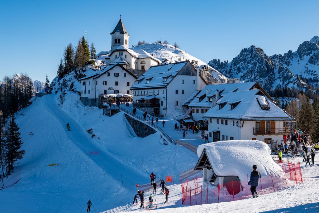 Village de montagne avec chapelle au sommet dans les Dolomites italiennes, sommets escarpés et sapins enneigés